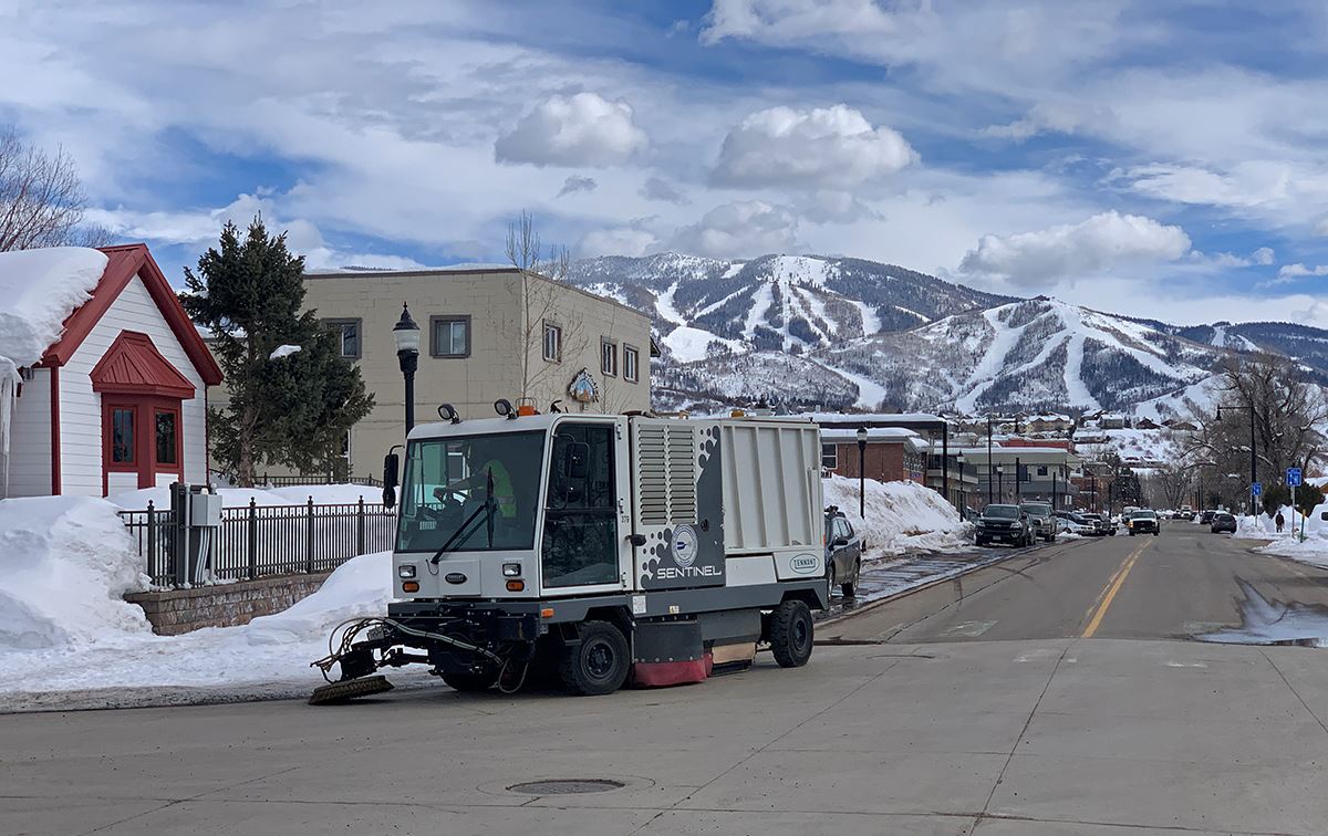 A street sweeper cleans up debris on a city street, with nice views of snowy Mt Werner